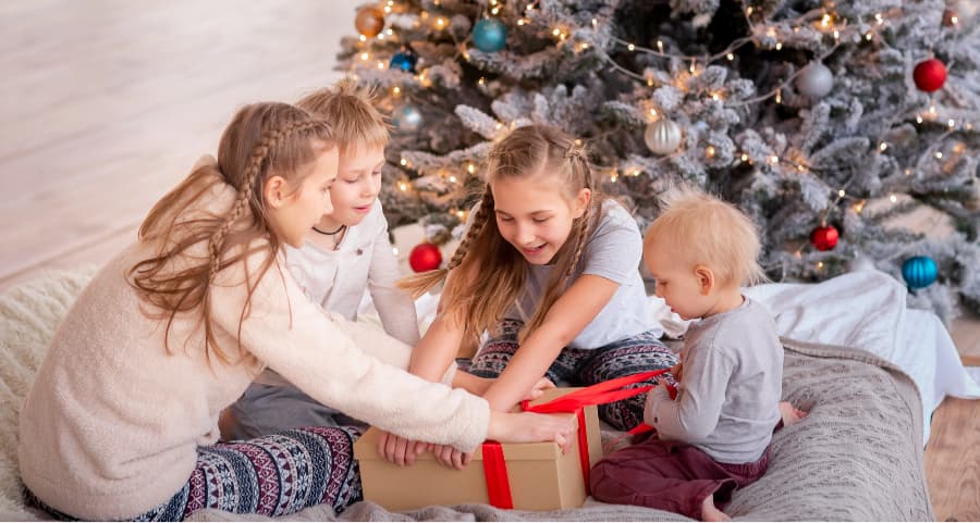 Siblings opening a present in the family room near a Christmas tree.